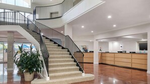 Eine geräumige Lobby mit einer geschwungenen Treppe, einem Empfangstresen und einer großen Pflanze.