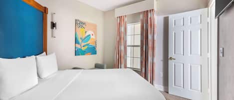 A hotel room with a bed, a ceiling fan, a painting on the wall, a window with curtains, and a door.