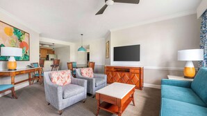 Ein modernes Wohnzimmer mit zwei grauen Sesseln, einem blauen Sofa, einem Holztisch und einem an der Wand befestigten Fernseher.