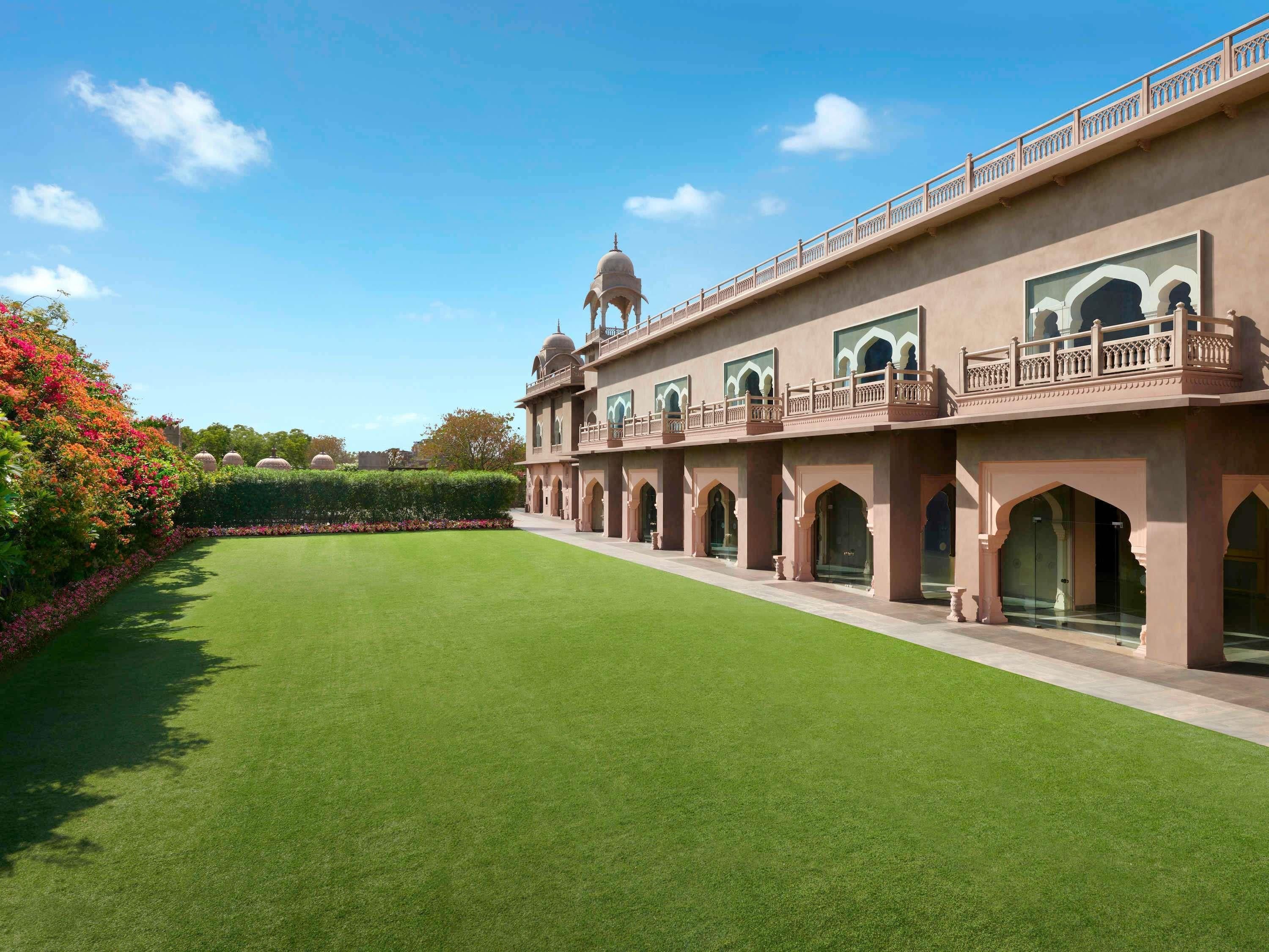 A large building with multiple arched windows and a central dome, surrounded by well-maintained lawns and flowering plants.