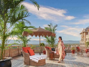 Una terraza con mobiliario de mimbre, un paraguas grande y vistas a un edificio lejano.
