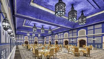 A large banquet hall with multiple round tables, chandeliers, and a patterned carpet.