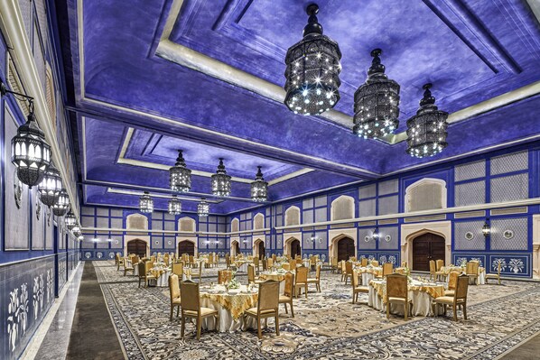 Un gran salón de banquetes con varias mesas redondas, candelabros y una alfombra estampada.