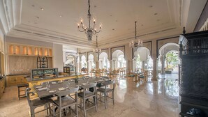 A spacious dining area with a long table, multiple chairs, and a central bar area with a display case. - Fairmont Jaipur (Amer)