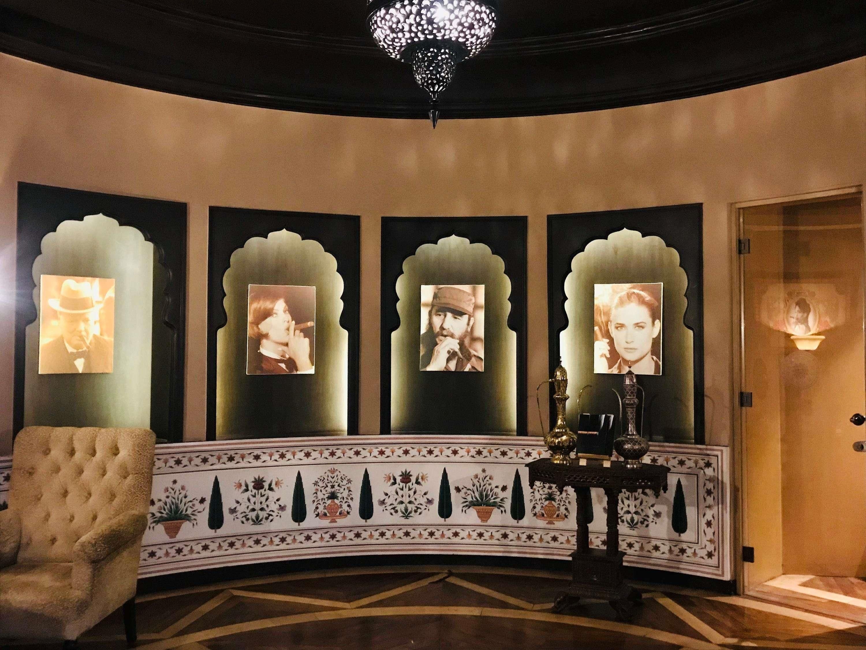 A lobby with a tufted armchair, a decorative table, and framed photographs on the wall.