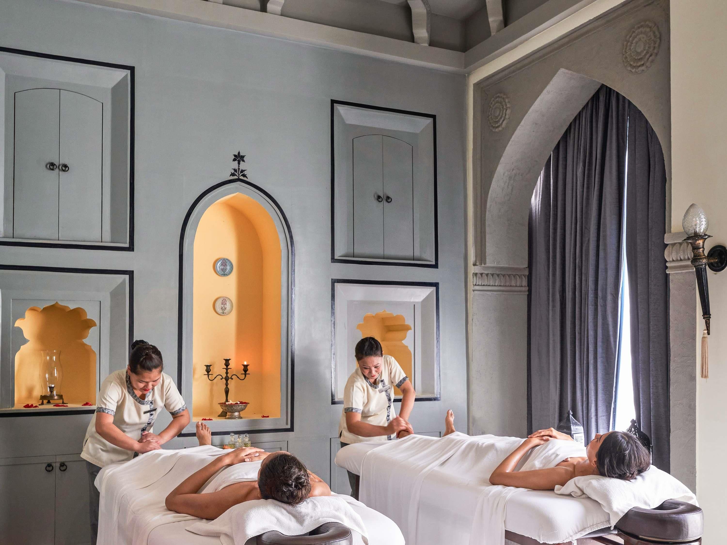 A spa room with two massage tables, a mirror, and a decorative archway.