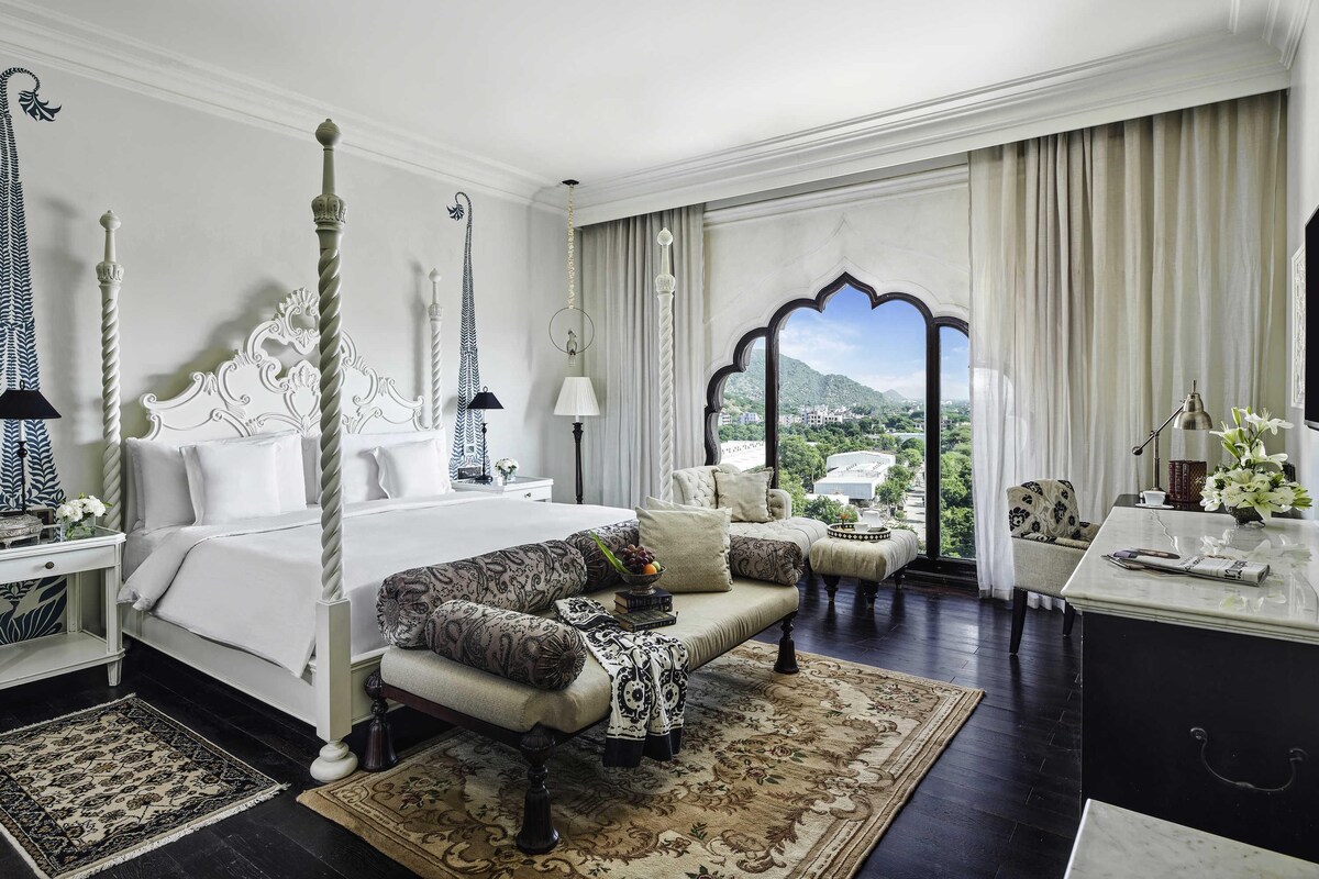 A four-poster bed, a sofa, a chair, a desk, and a view of a mountainous landscape.