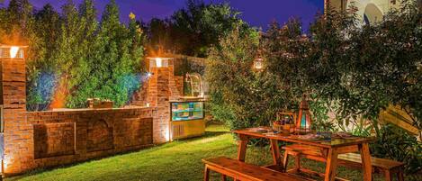 An outdoor patio with a brick barbecue area, a wooden table with benches, and a decorative lantern.