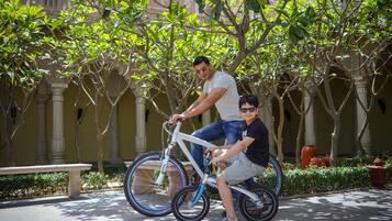 Un hombre y un niño en una bicicleta blanca en un patio con columnas y follaje.