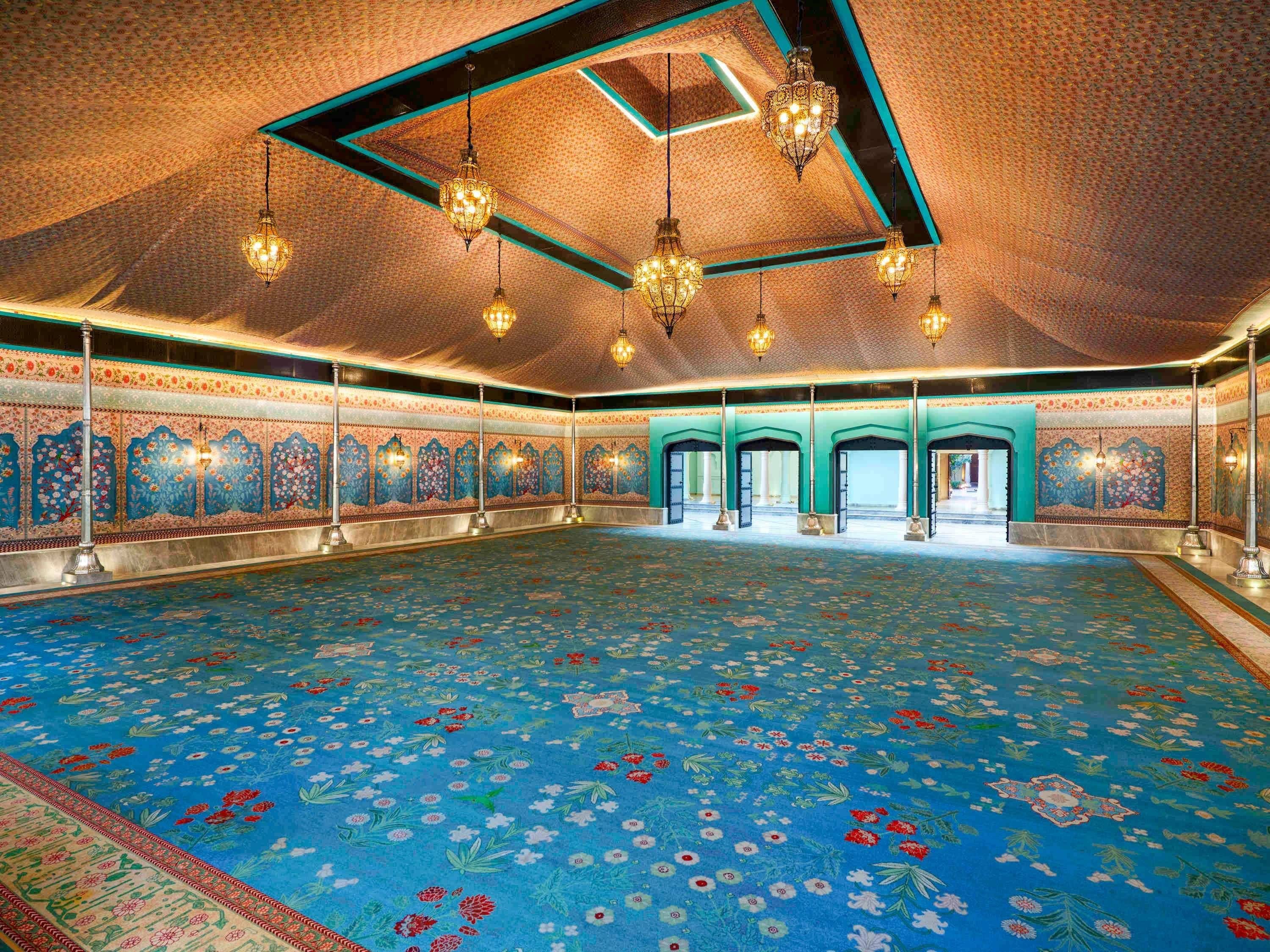 A large hall with a patterned carpet, ornate wall decorations, and hanging chandeliers.