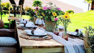 Une table en bois, mise avec des assiettes, des couverts et des sets de table en fibres tressées, agrémentée de divers bouquets de fleurs et de paniers.