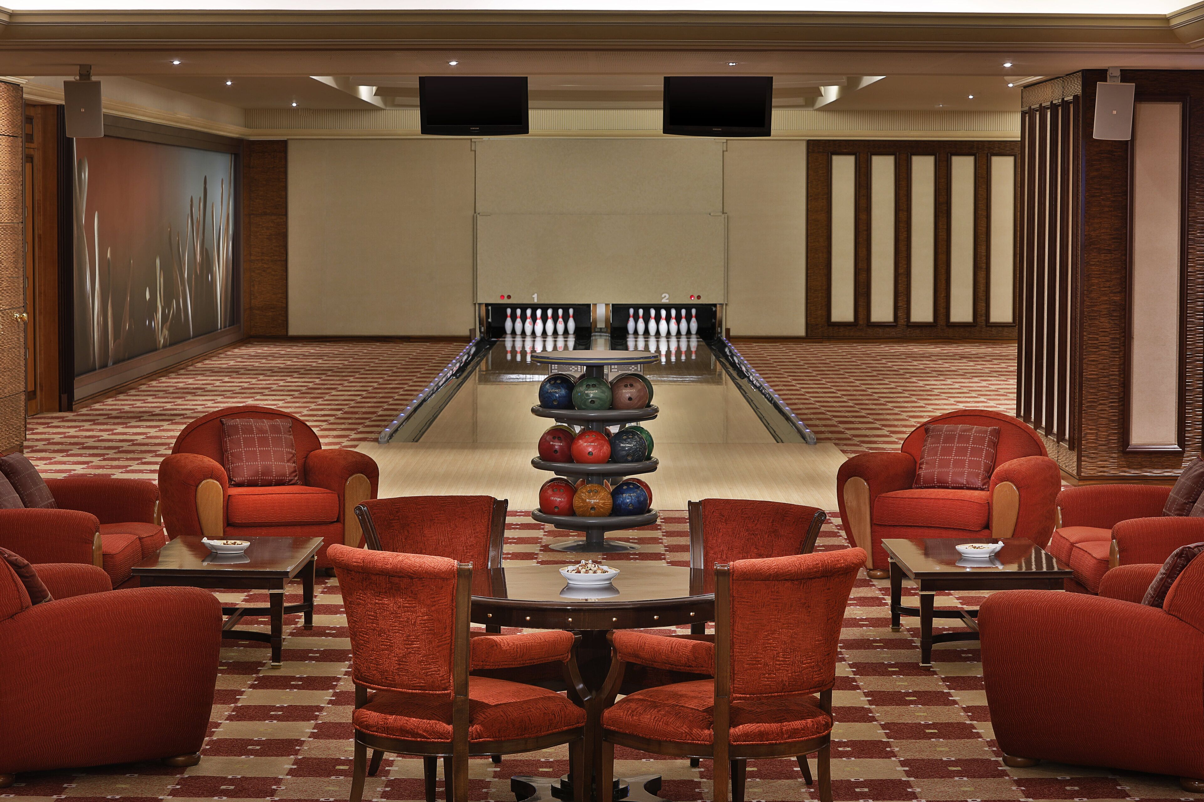A bowling alley with red chairs and tables, a bowling lane, and two televisions on the wall.
