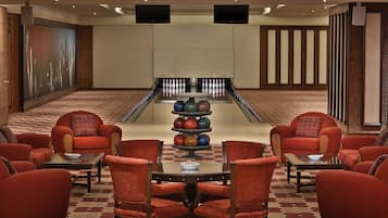 A bowling alley with red chairs and tables, a bowling lane, and two televisions on the wall.