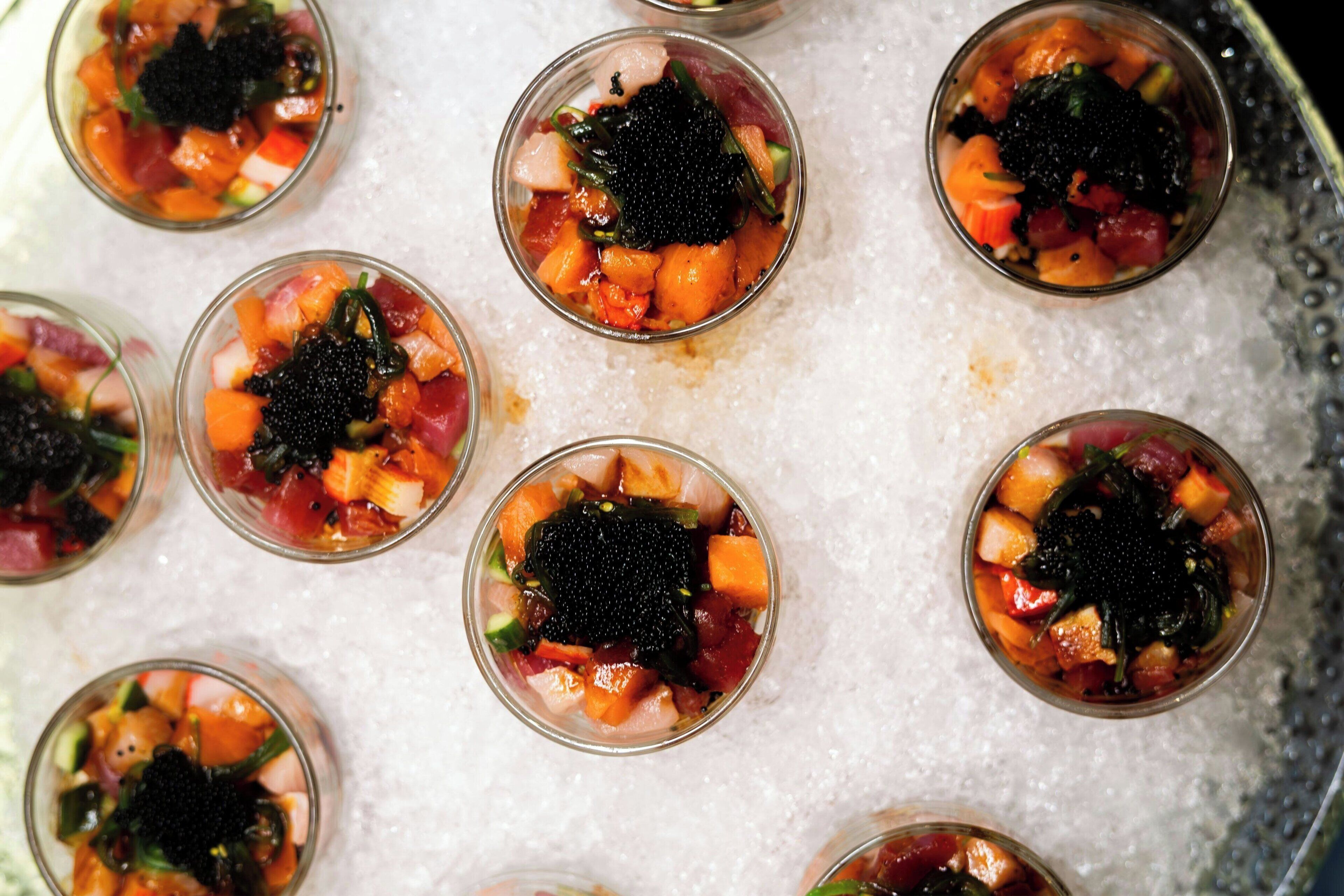 Una bandeja con copas pequeñas que contienen un plato de mariscos con diferentes verduras y caviar negro.