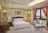 A hotel room with a large bed, a chair, a desk, a lamp, and a window with curtains.