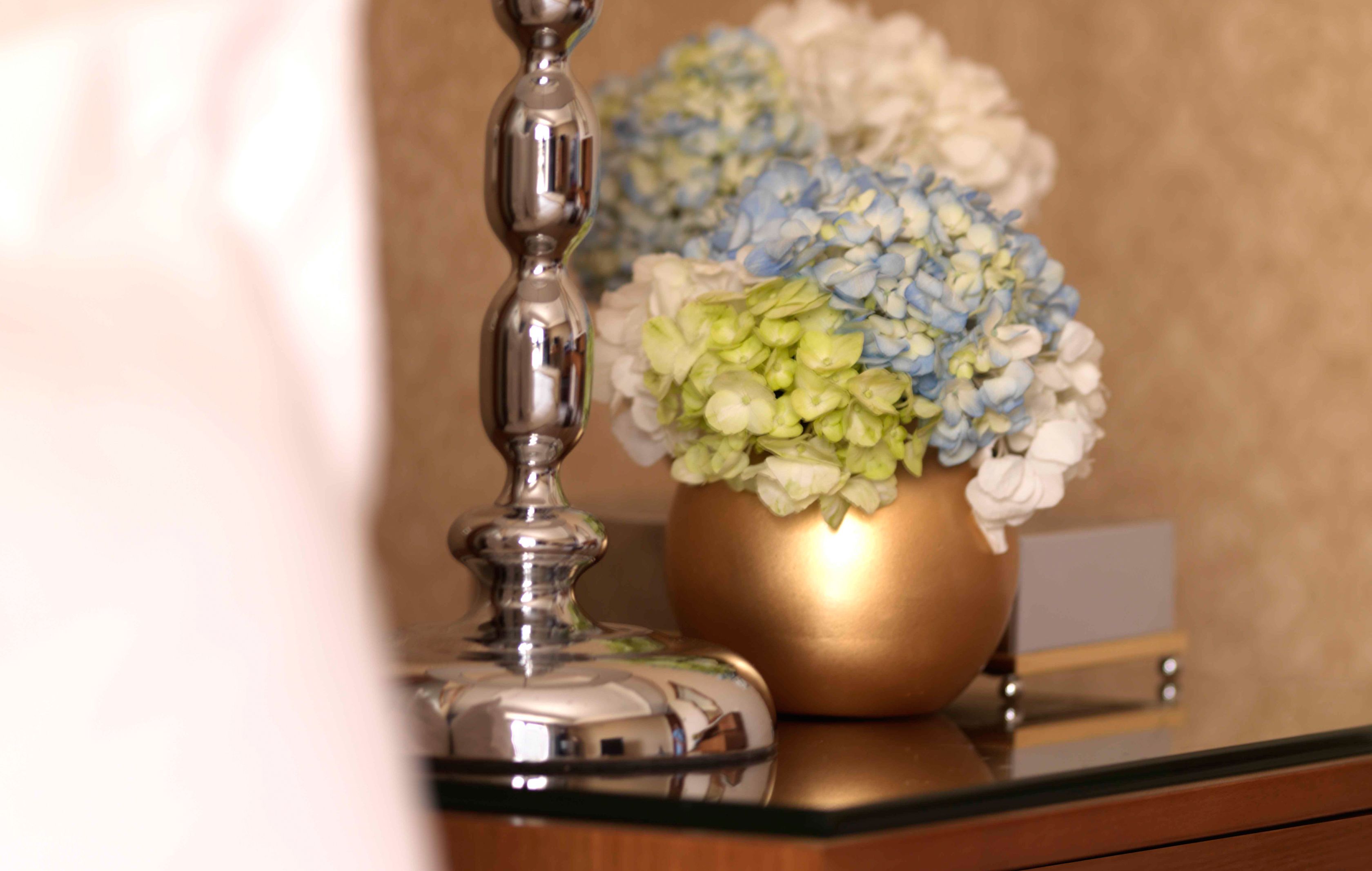 A gold vase with blue and white flowers on a reflective surface.
