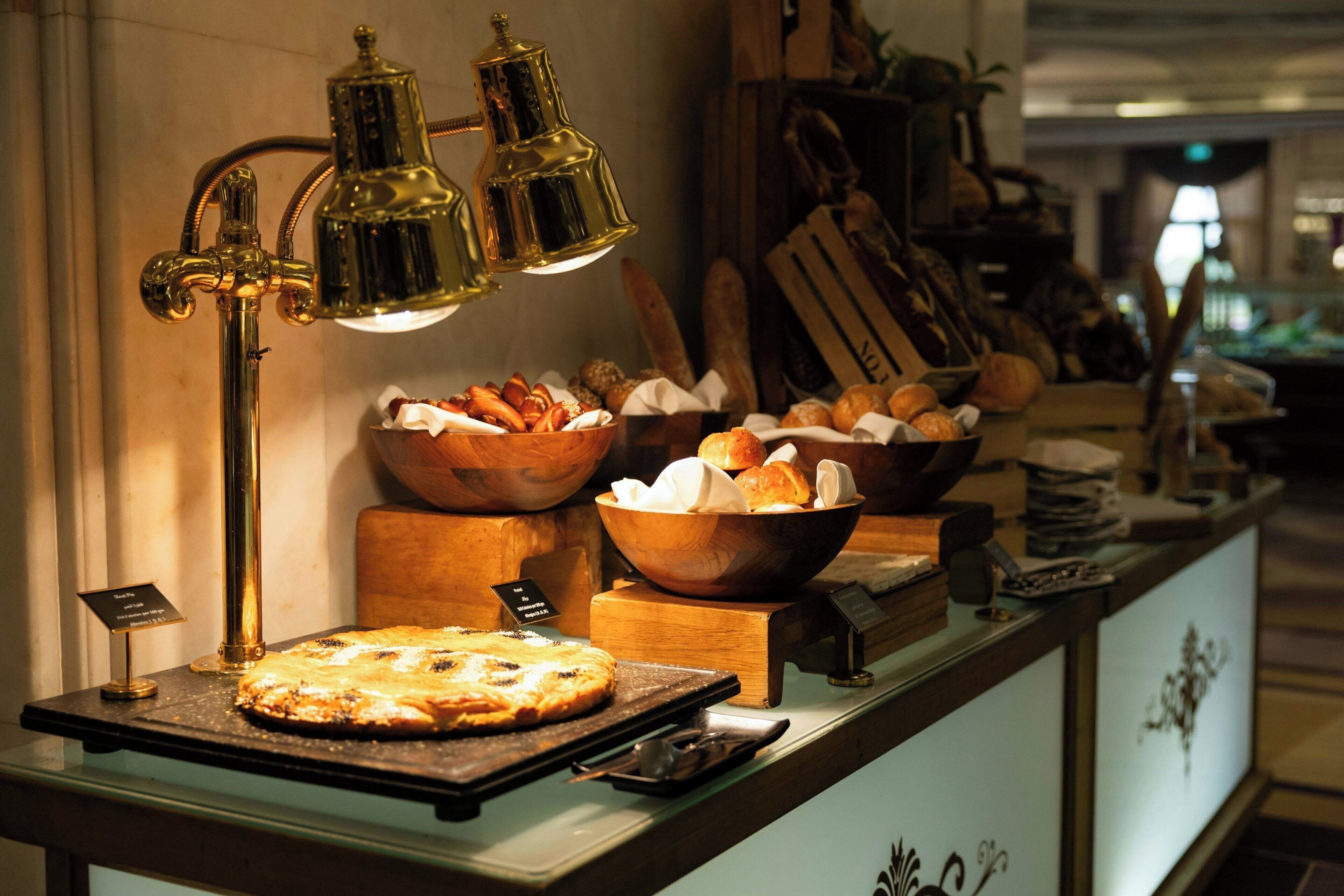 Ein Frühstücksbuffet mit Brot, Gebäck und Pizza, beleuchtet von einer Messinglampe.
