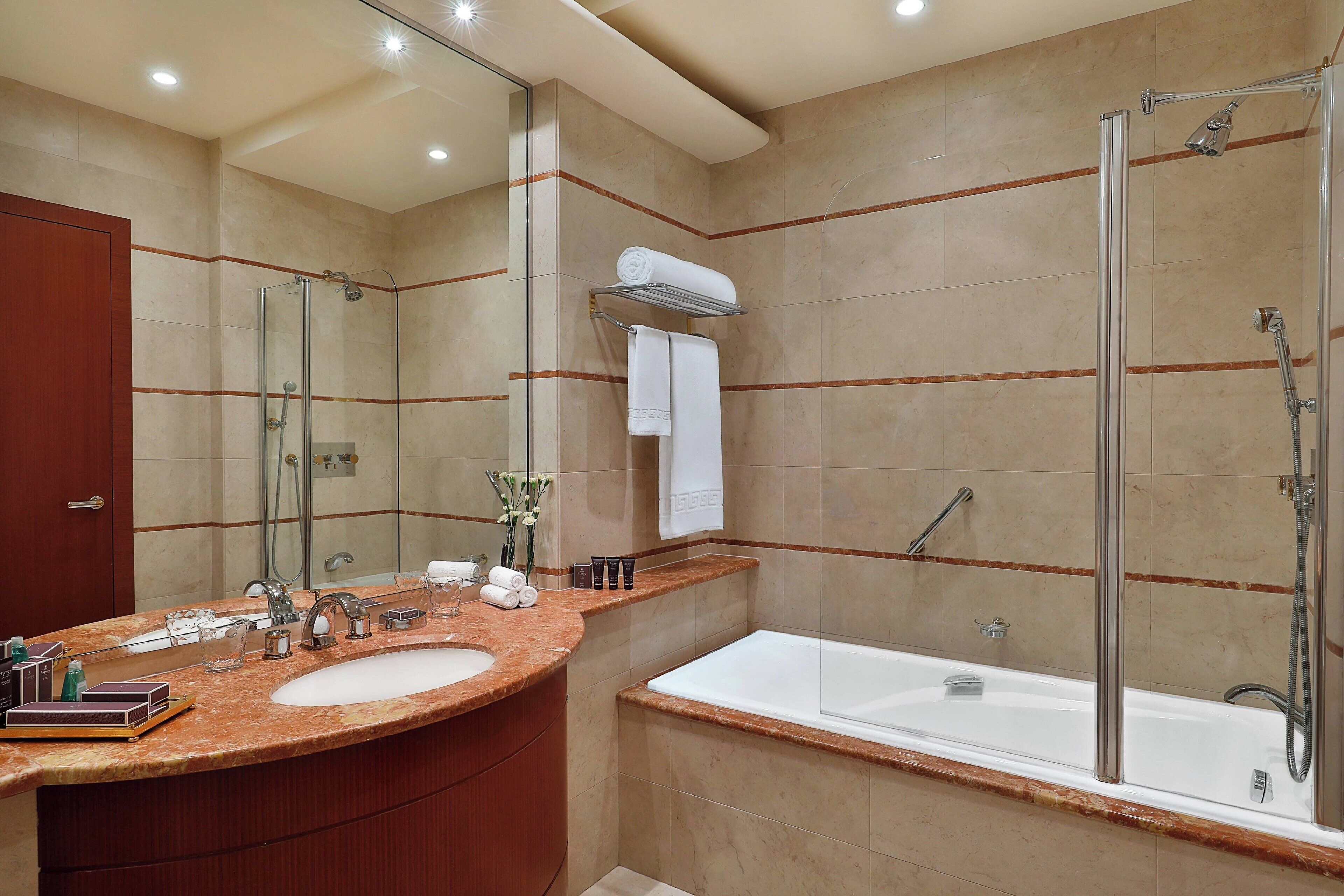 Un baño moderno con lavamanos de mármol, ducha con mampara de vidrio y una bañera grande.