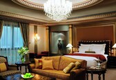 A luxurious hotel room with a large bed, a sofa, a coffee table, and a chandelier.