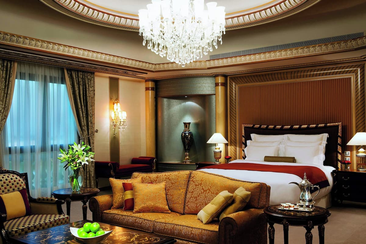 Um quarto de hotel luxuoso com uma cama grande, um sofá, uma mesa de centro e um candelabro.