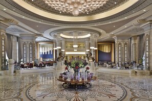 A grand lobby with a central floral arrangement, high ceilings with intricate designs, and a polished marble floor.