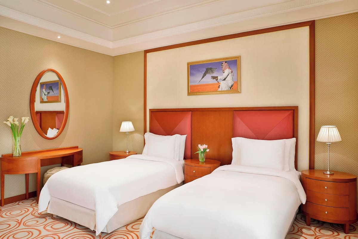 Quarto de hotel com duas camas, um espelho grande, um quadro e um tapete estampado.
