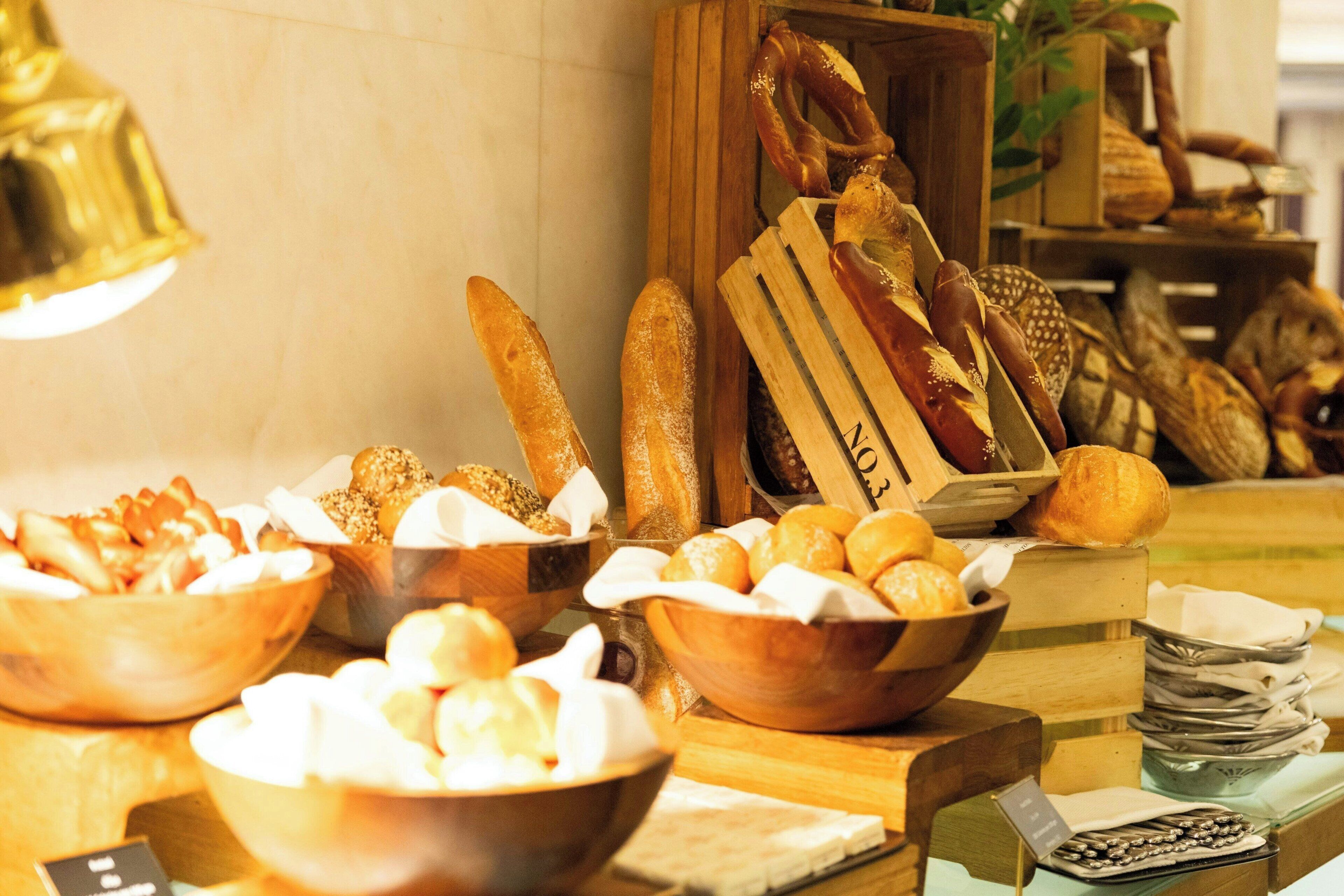 A variety of breads and pastries displayed on a wooden counter with a bell in the background.