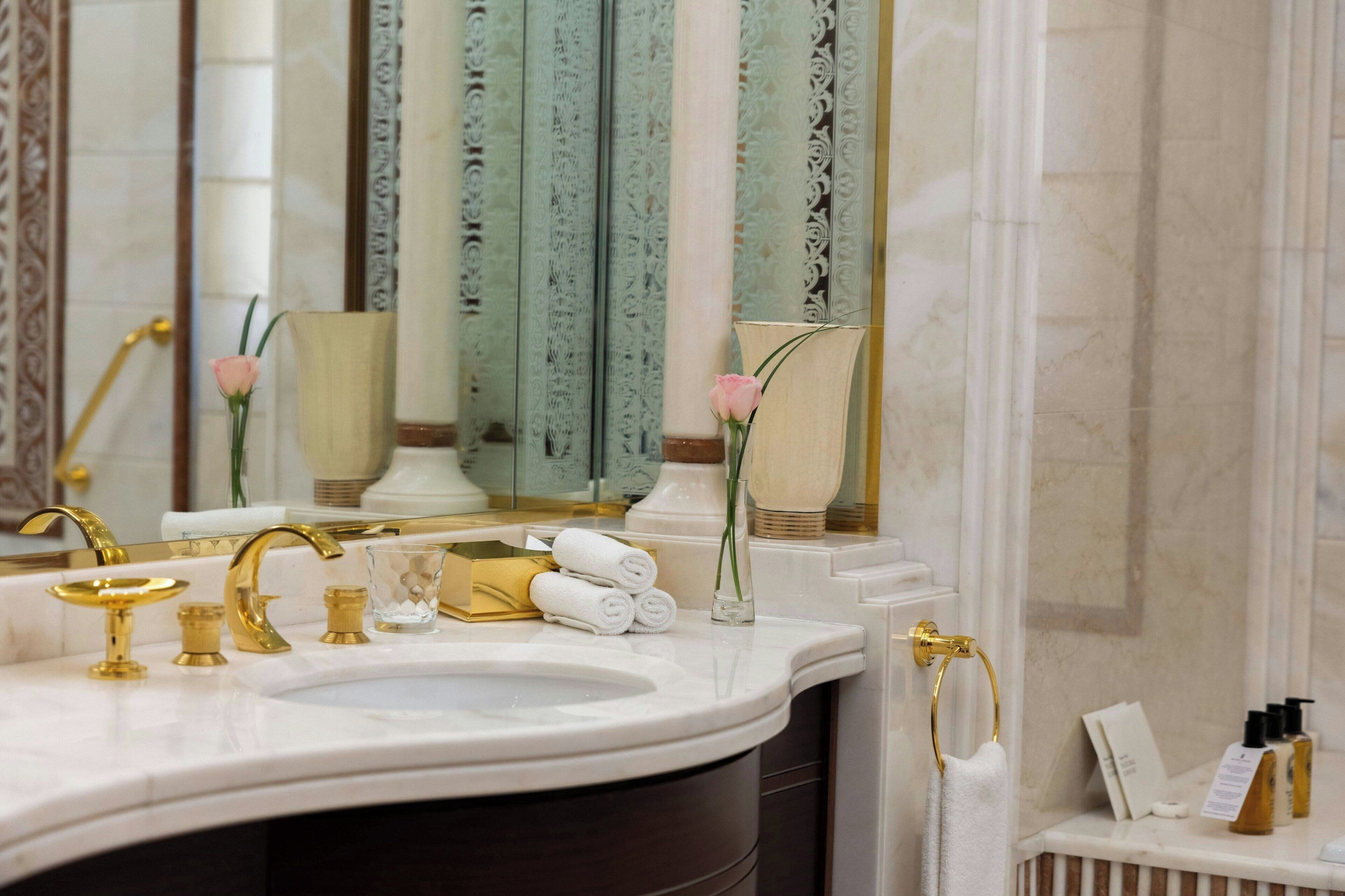 A bathroom with a marble sink, gold fixtures, a mirror, and a towel rack.
