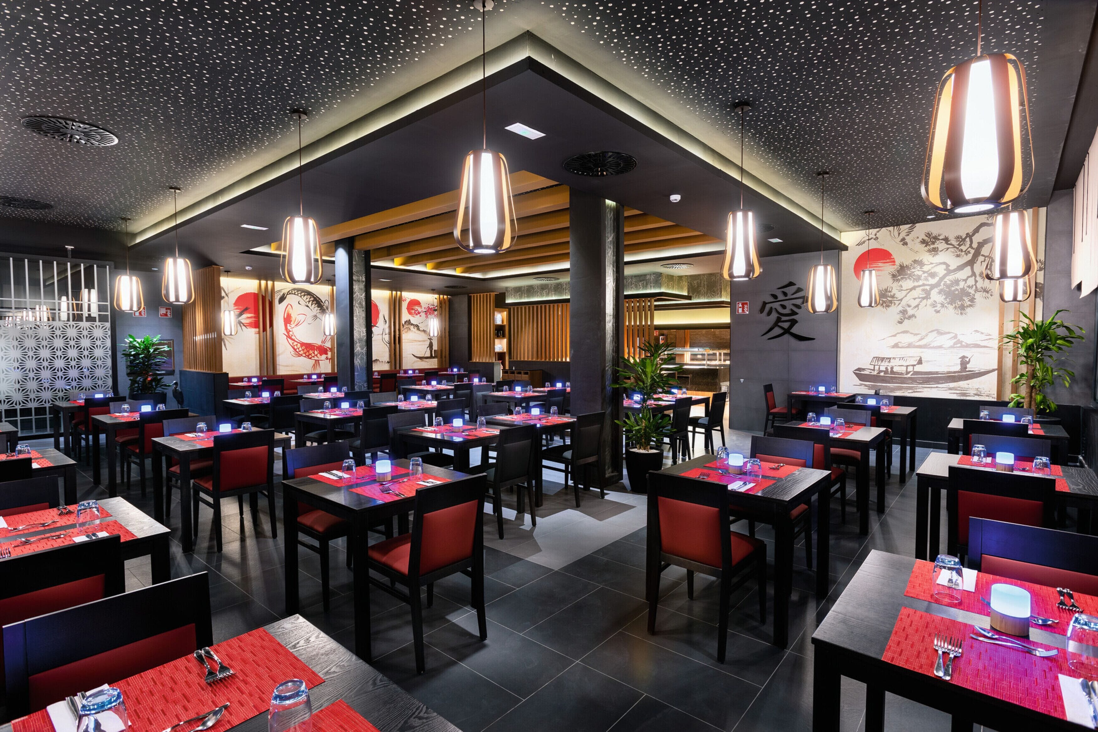 Een restaurant met meerdere tafels, rode en zwarte stoelen, en hangende吊灯.