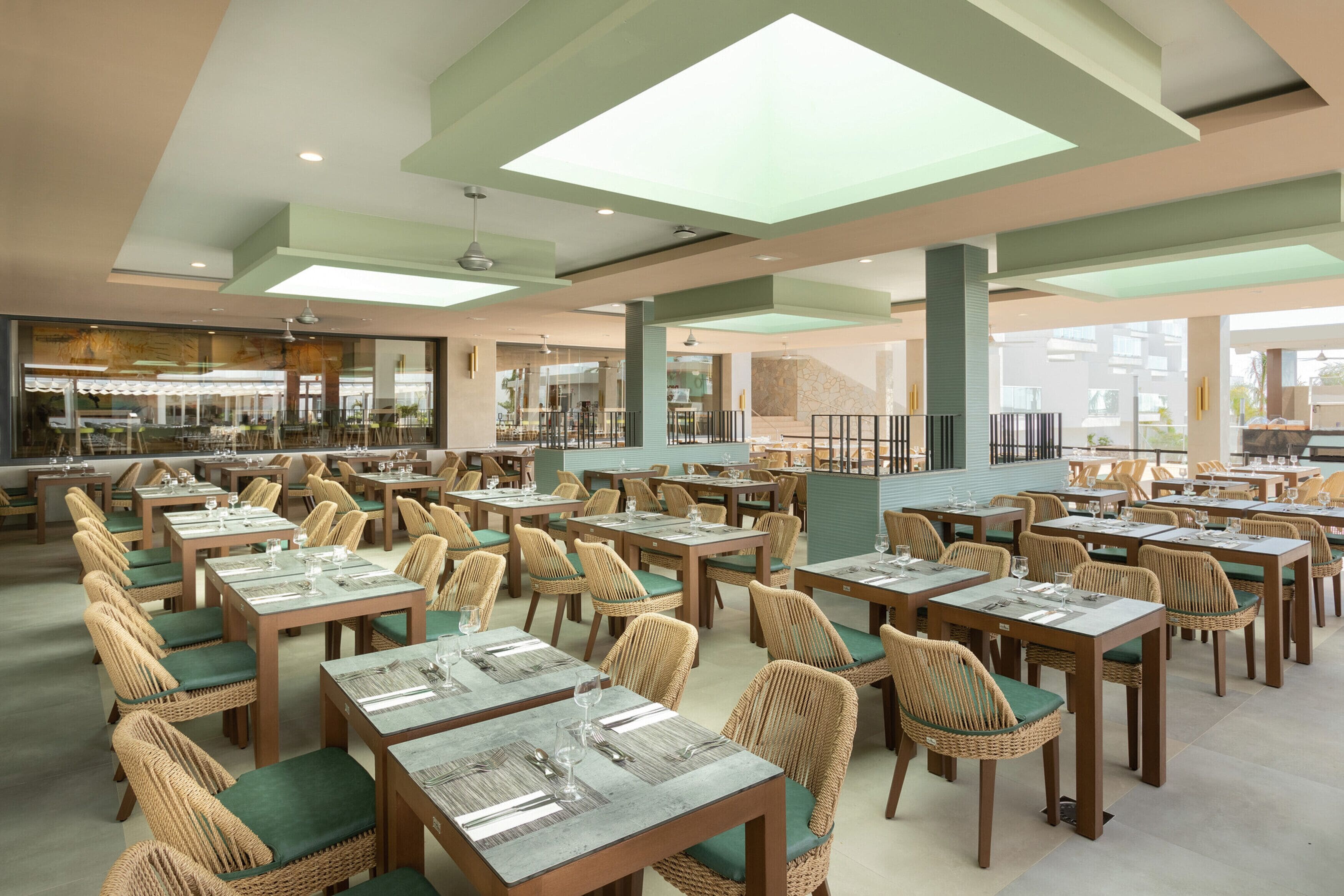 Un restaurant spacieux, doté de nombreuses tables et chaises, de grandes fenêtres et d’un plafond au design moderne.