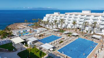 A resort with multiple swimming pools, palm trees, and a view of the ocean.
