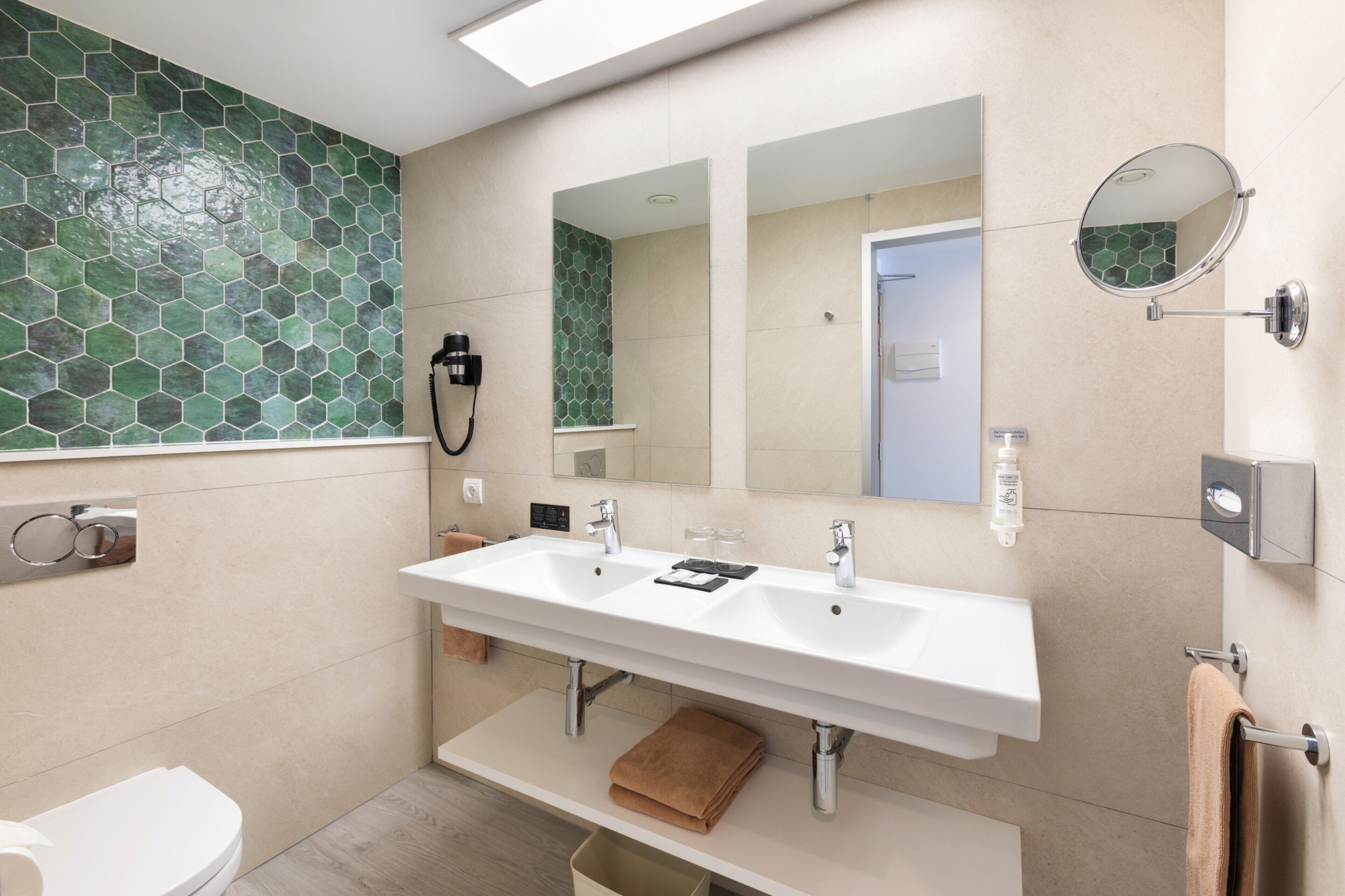 A modern bathroom with a large white sink, two mirrors, and a green mosaic tile backsplash.