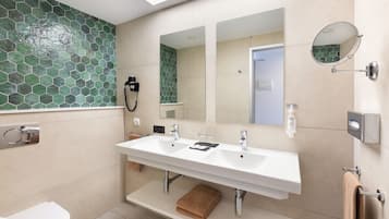 A modern bathroom with a large white sink, two mirrors, and a green mosaic tile backsplash.