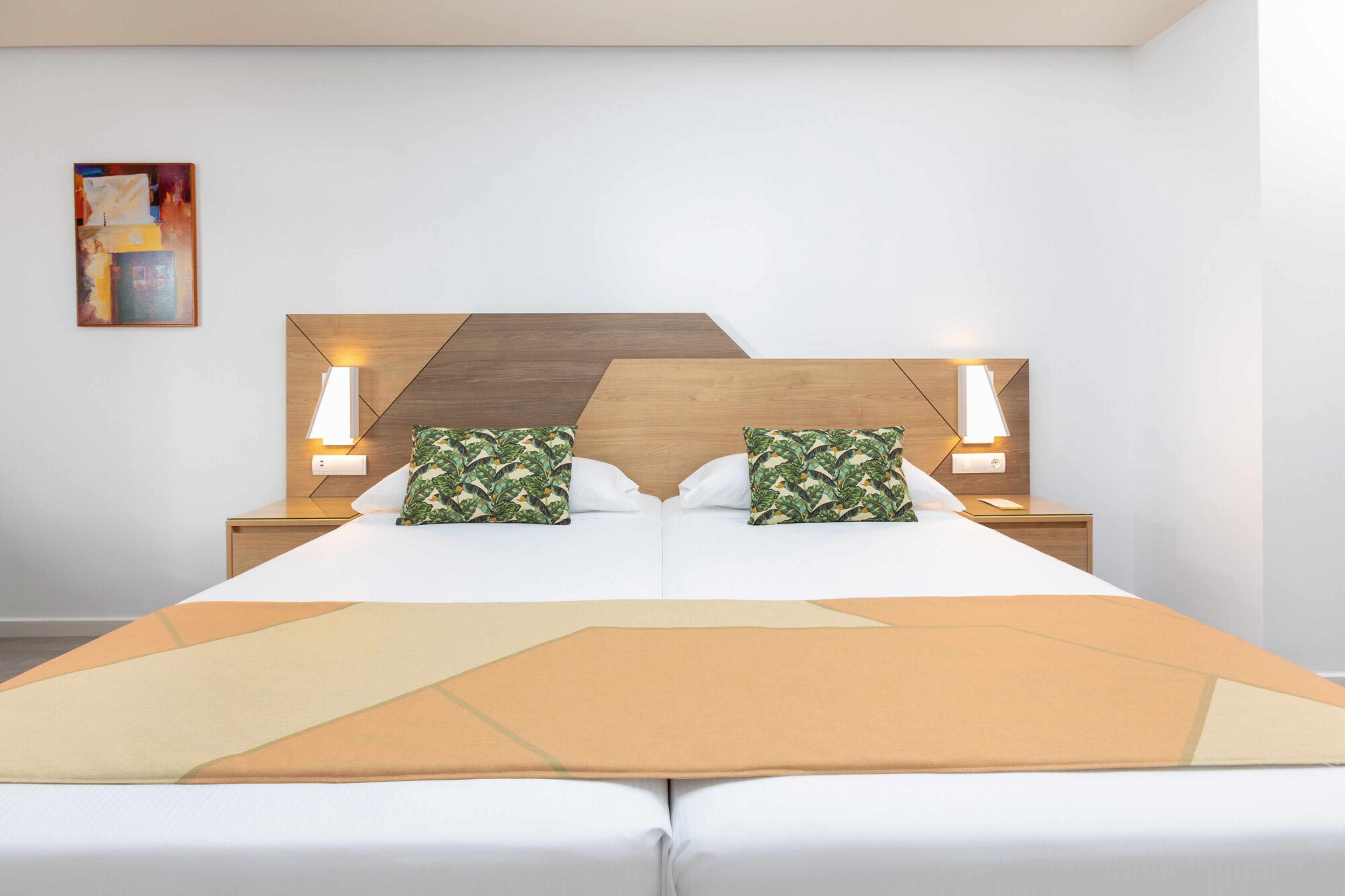 Quarto de hotel moderno com uma cama grande, duas mesas de cabeceira e um cobertor com padrão geométrico.