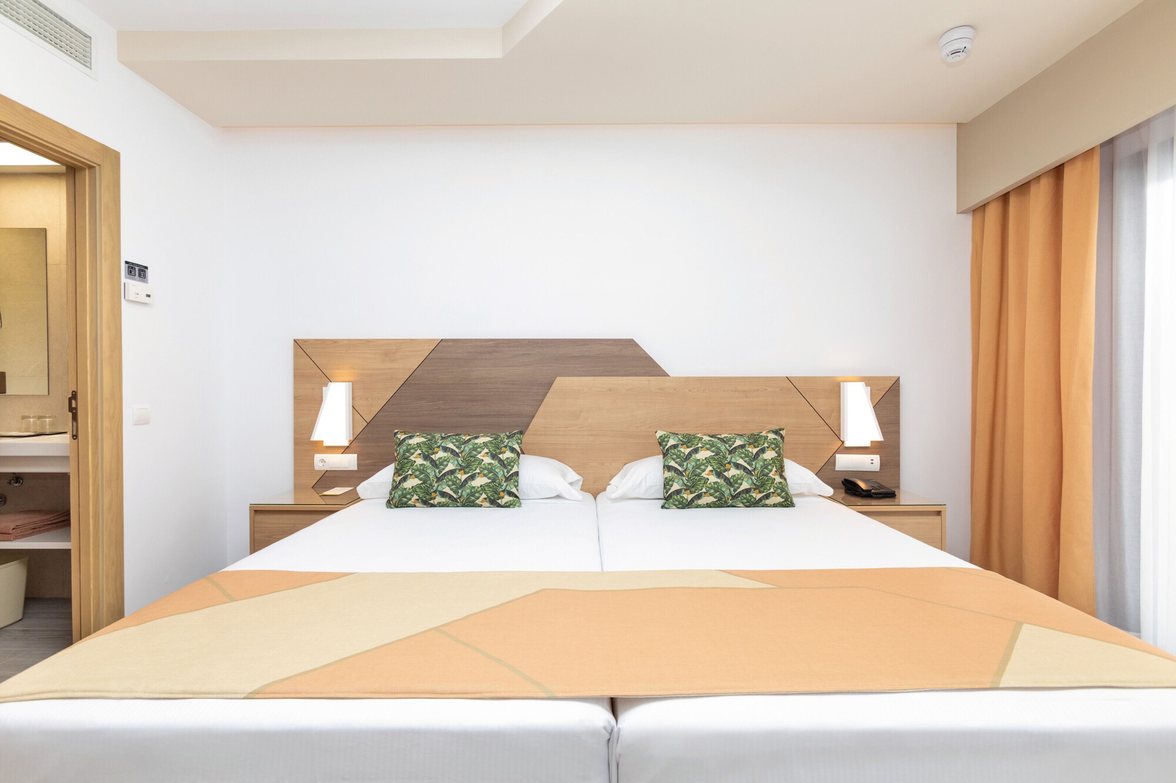 Habitación de hotel con una cama grande, dos mesitas de noche, un cabecero de madera y una ventana con cortinas.