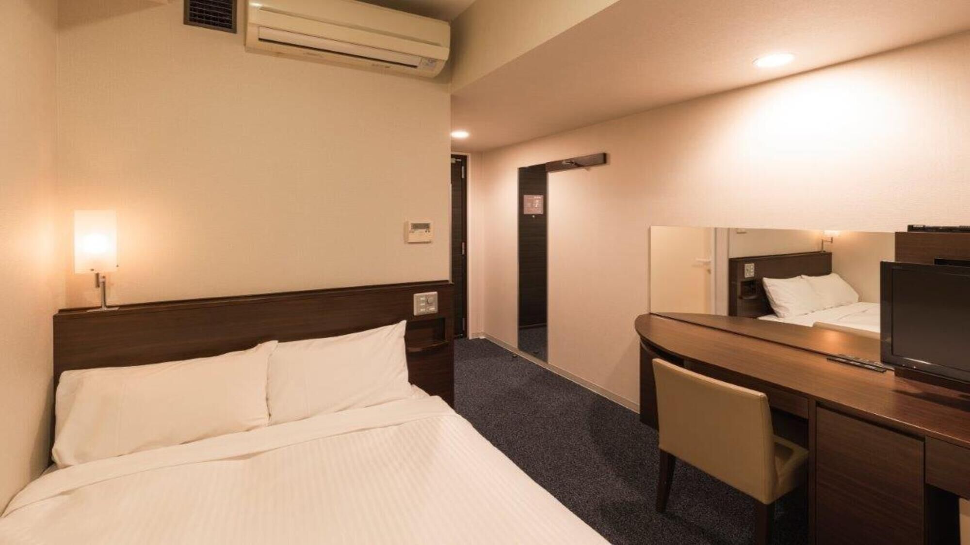 Een hotelkamer met een bed, een bureau, een stoel, een televisie en een spiegel.