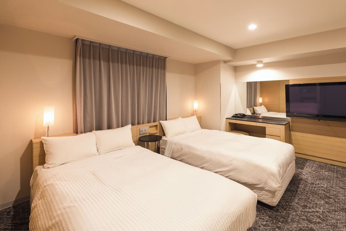 A hotel room with two beds, a desk, a TV, and a nightstand.