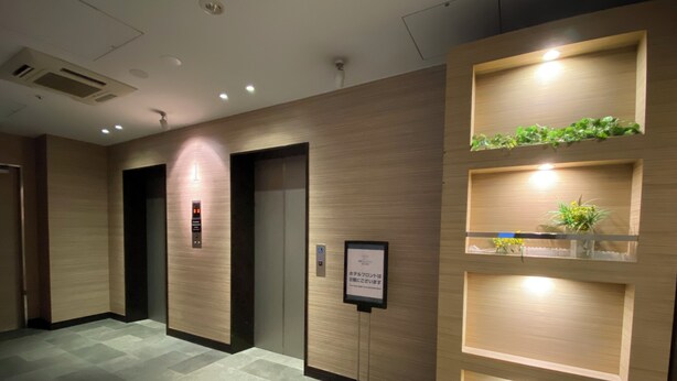 A modern hotel lobby with a reception desk, two elevators, and a wall-mounted information board. - Sotetsu Fresa Inn Tokyo Kyobashi (Tokyo)