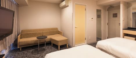 Habitación de hotel con dos camas, un sofá, una mesita pequeña, un equipo de aire acondicionado y un televisor.