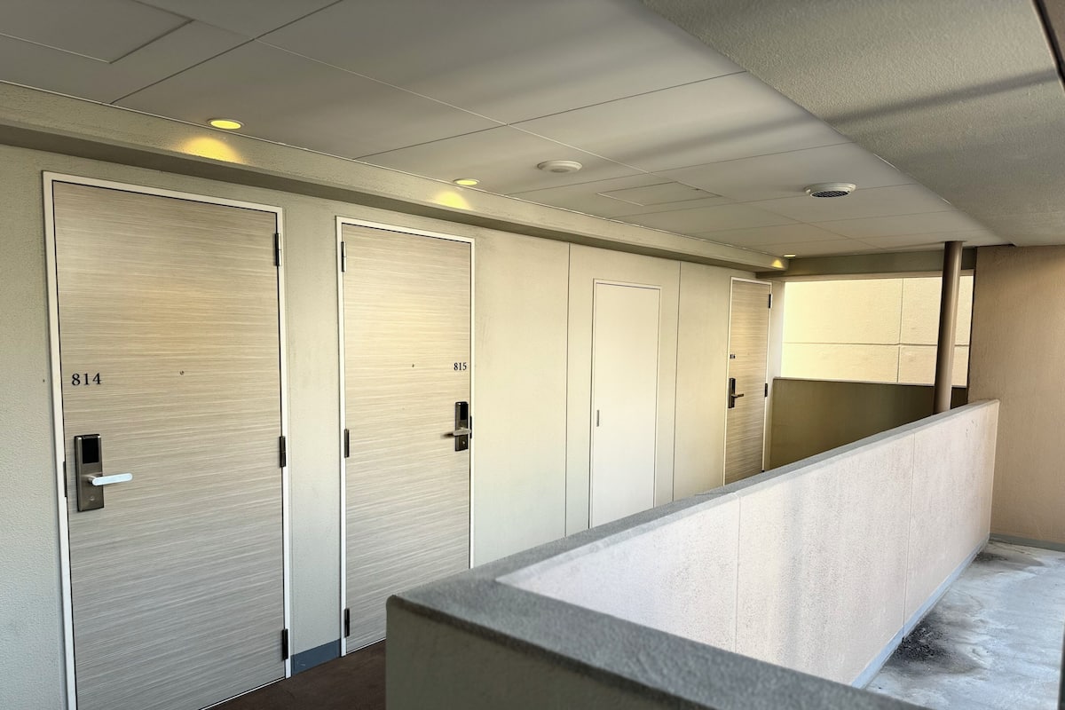 A corridor with closed doors numbered 814 and 815, a concrete bench, and a ceiling with recessed lighting.
