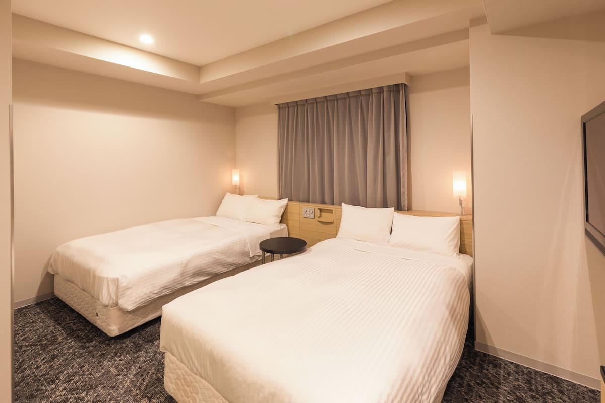 A hotel room with two single beds, a small round table, and a large window with curtains.