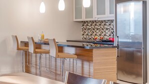 A modern kitchen with a central island, bar stools, a refrigerator, and pendant lighting.