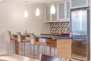 A modern kitchen with a central island, bar stools, a refrigerator, and pendant lighting.