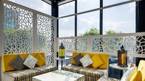 Un espace de détente extérieur moderne, avec des canapés à rayures et une table basse en verre, entouré de panneaux décoratifs en treillis et de deux lanternes.