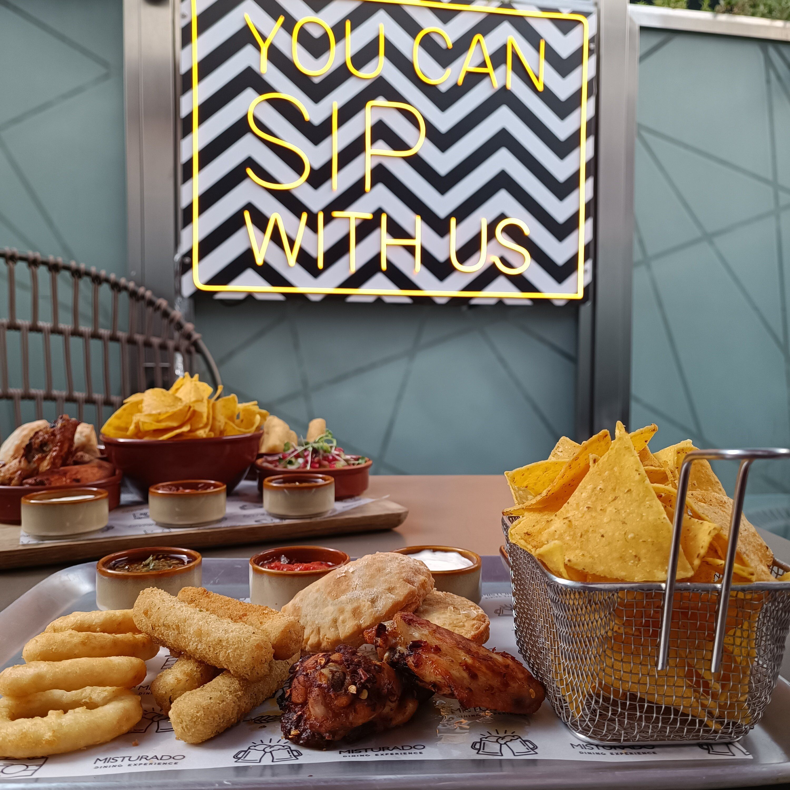 A dining table with various food items including nachos, fried chicken, and chips, along with small bowls of dipping sauces.