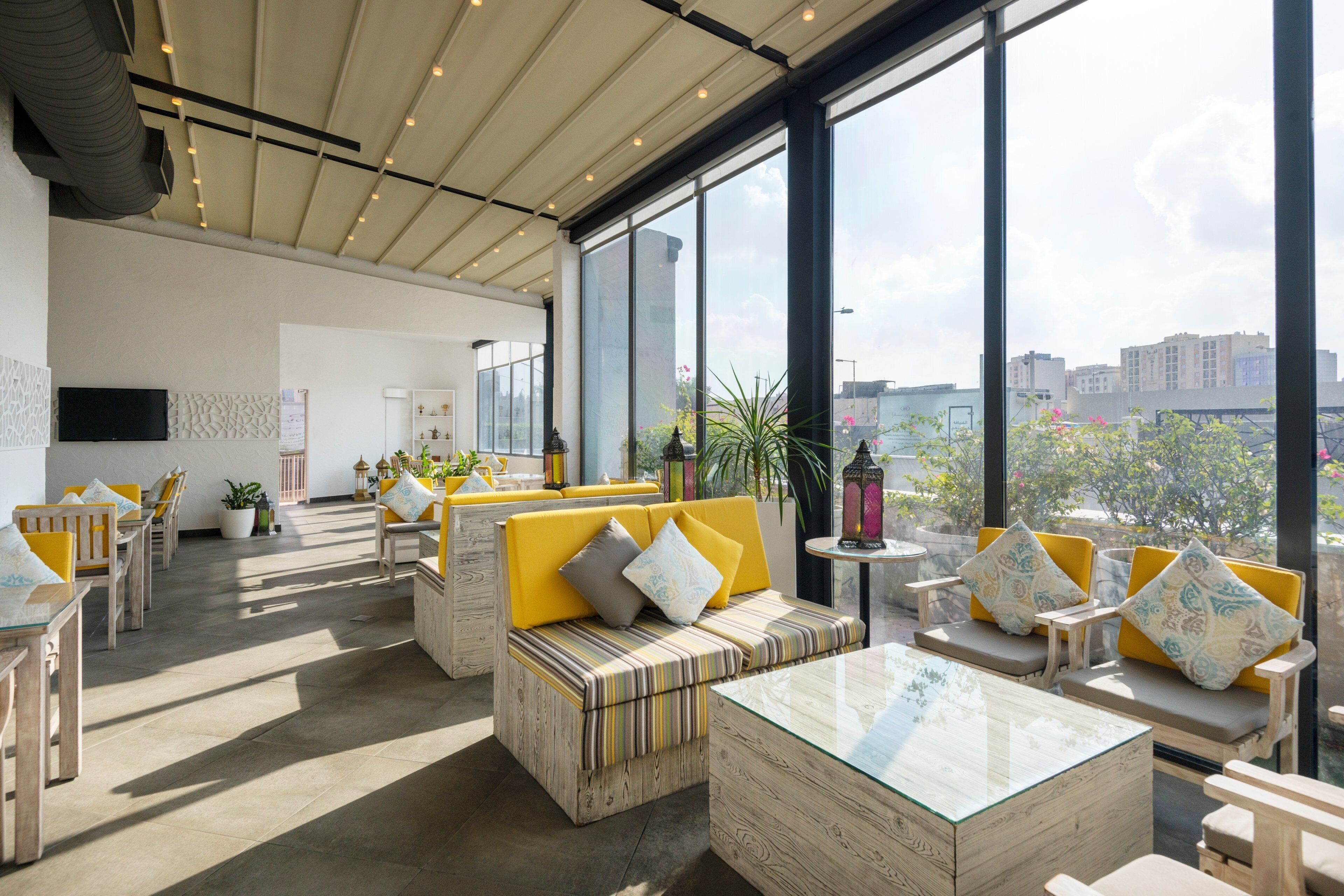 Interior moderno com pé direito alto, janelas amplas e área de estar com almofadas e mesa de centro de vidro.
