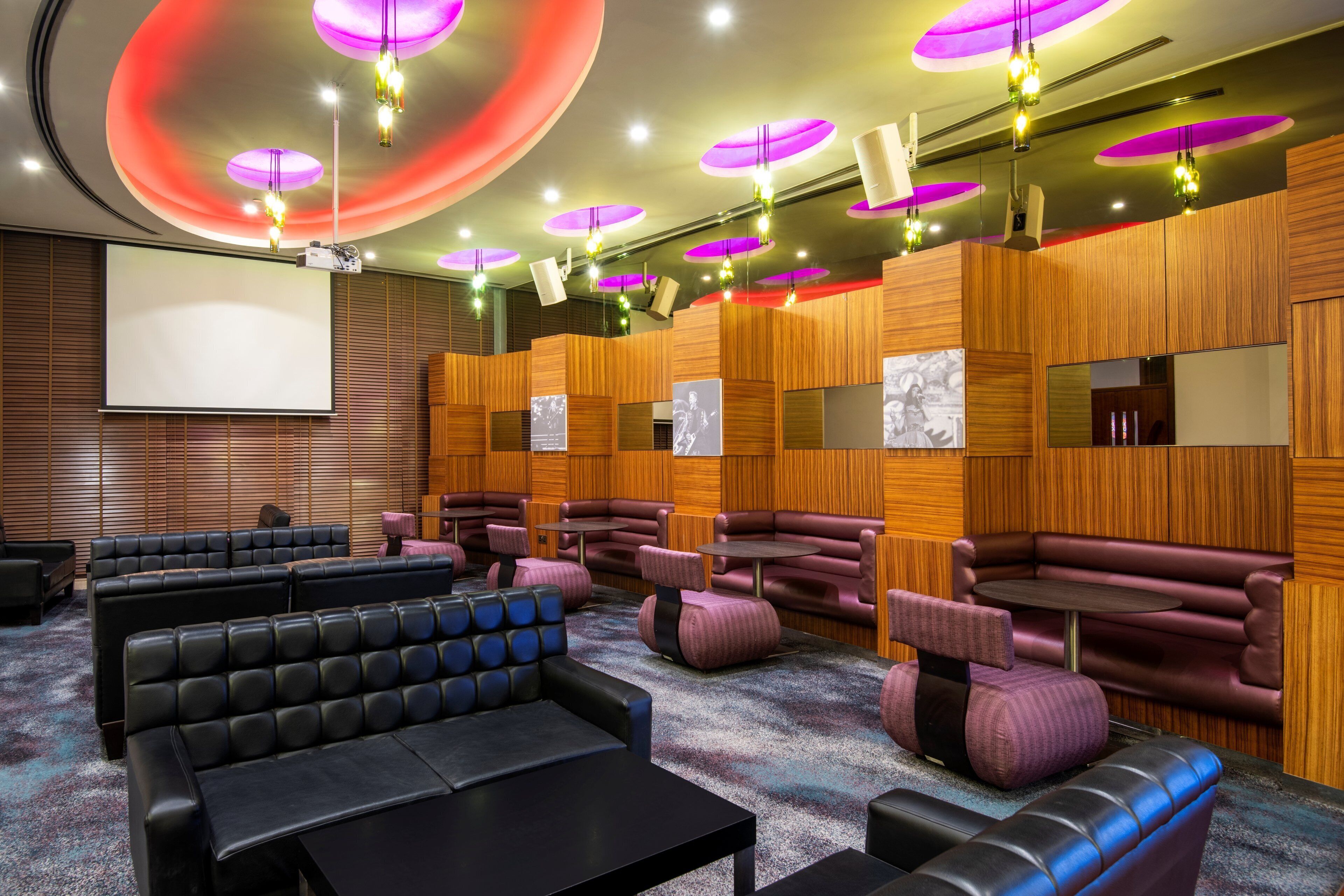 A modern cinema with black and purple seating, wooden paneling, and a large screen.