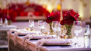 A table set with plates, cutlery, and glasses, adorned with white flowers and red roses in a geometric vase.