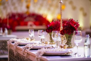 A table set with plates, cutlery, and glasses, adorned with white flowers and red roses in a geometric vase.