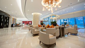 A modern hotel lobby with a curved ceiling, a reception desk, and seating areas with round tables.